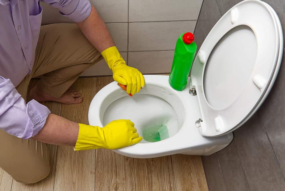 Personne nettoyant avec soin la base d'une cuvette de WC pour éliminer une odeur d'ammoniaque.