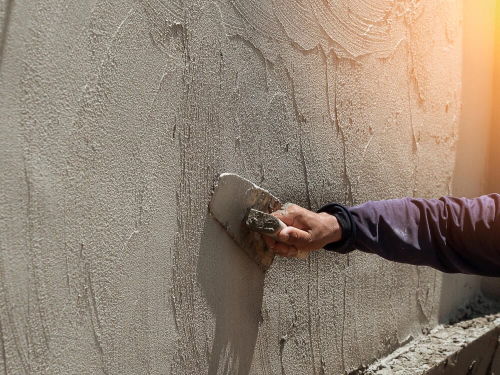 Main d'un maçon appliquant du mortier-colle sur un muret avant de poser une couvertine en béton.