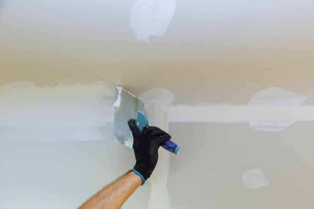 Joint acrylique en cours de lissage pour boucher un espace entre une plaque de Placo et le plafond.