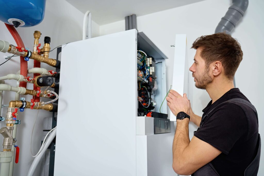 Technicien chauffagiste vérifiant les composants internes d'une chaudière à gaz lors d'une révision annuelle.