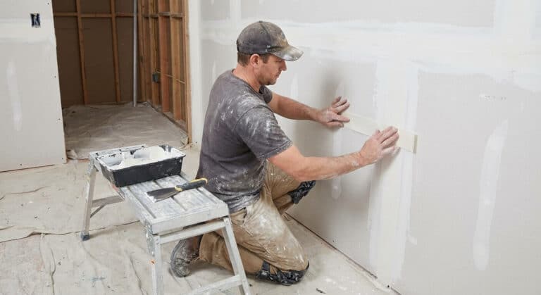Plaquiste appliquant une bande de papier à joint sèche directement sur l'enduit frais d'une cloison