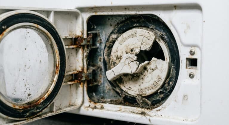 Accueil 1 Gros plan sur un bouchon de vidange de machine à laver dont la poignée en plastique est brisée, situé derrière la trappe de service.
