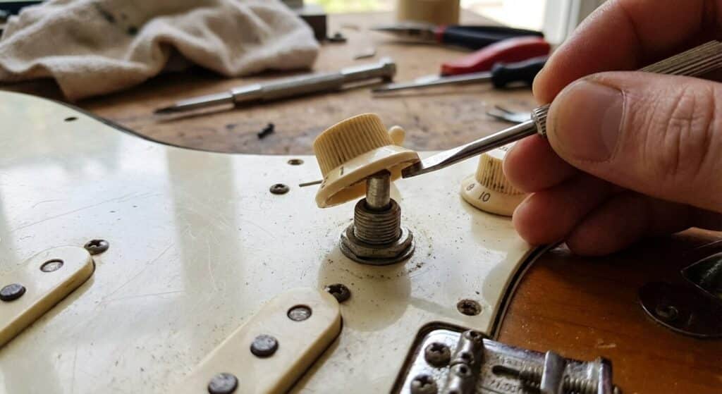 Gros plan sur le démontage du bouton de volume d'une guitare électrique pour accéder à l'axe du potentiomètre
