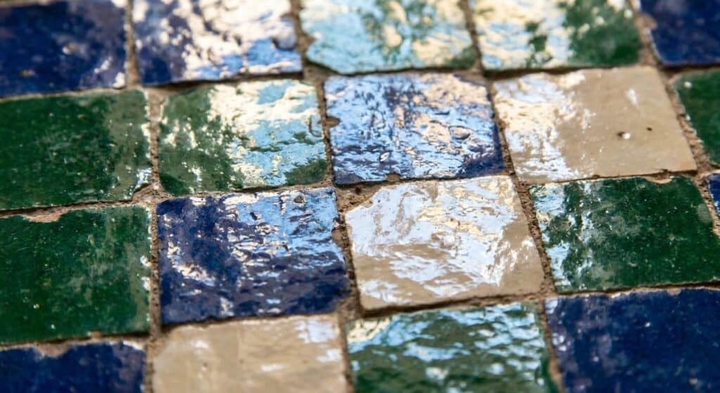 Gros plan sur les irrégularités et les reflets brillants d'un carrelage zellige marocain traditionnel.