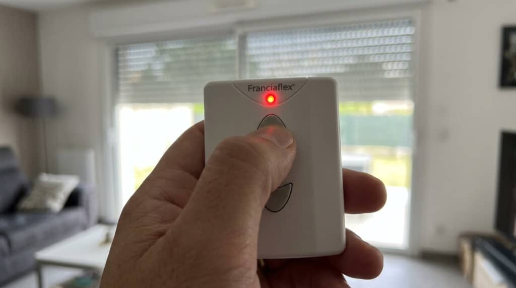 Télécommande de volet roulant Franciaflex tenue en main avec le voyant LED rouge actif.