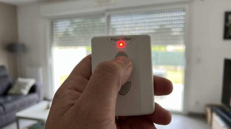 Télécommande de volet roulant Franciaflex tenue en main avec le voyant LED rouge actif.