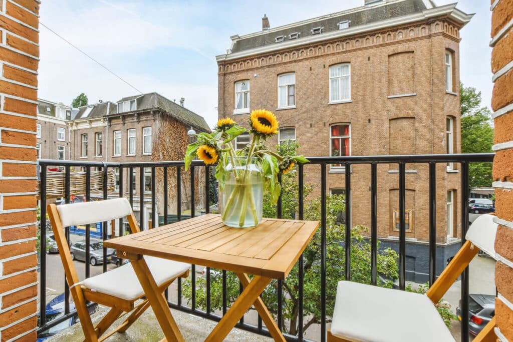 Un ensemble table et chaises pliantes en bois sur un petit balcon fleuri pour optimiser l'espace.