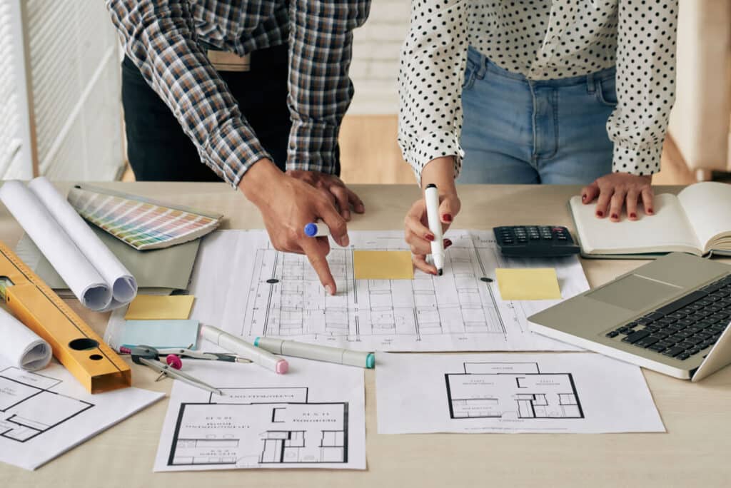 Une architecte d'intérieur analysant les plans de restructuration des cloisons et de luminosité pour un grand appartement.