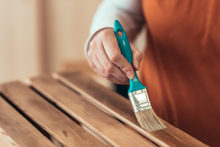 Une personne appliquant un solvant sur un volet en bois avec un pinceau pour enlever l'ancienne lasure.