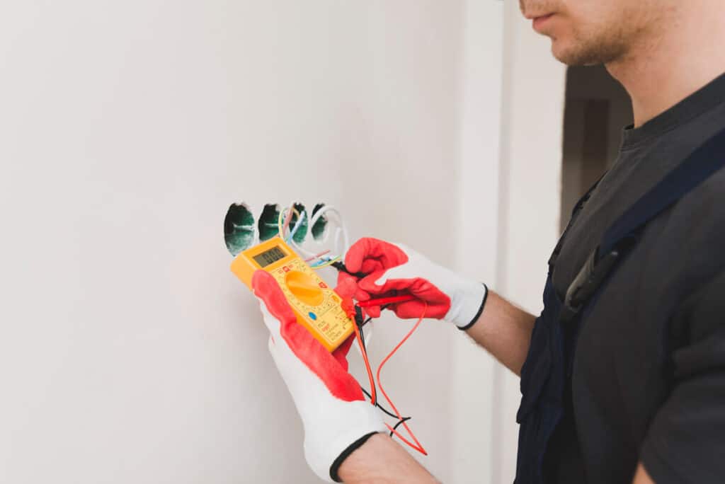 Un électricien mesurant la tension électrique d'une prise de courant à l'aide des pointes de touche d'un multimètre.