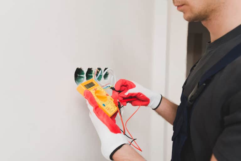 Un électricien mesurant la tension électrique d'une prise de courant à l'aide des pointes de touche d'un multimètre.