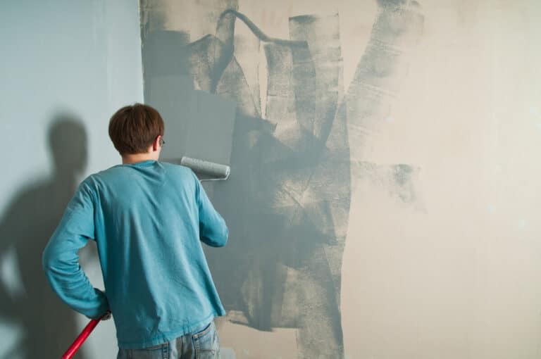 Une personne appliquant une couche de peinture mate au rouleau sur un ancien tissu tendu mural.