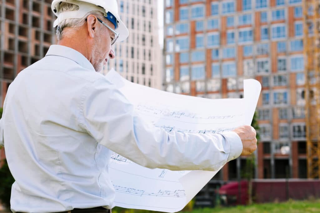 Un maître d'œuvre vendéen en train de contrôler les plans de construction sur un terrain à bâtir.