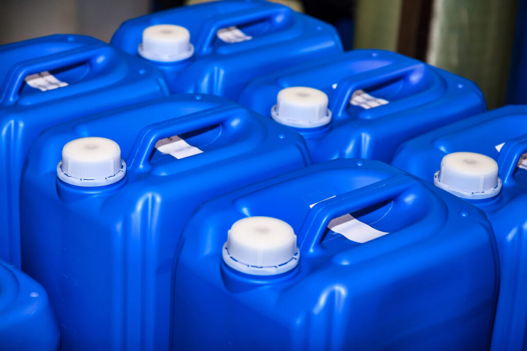 Différents bidons de produits de traitement d'eau stockés réglementairement dans un local technique de piscine.