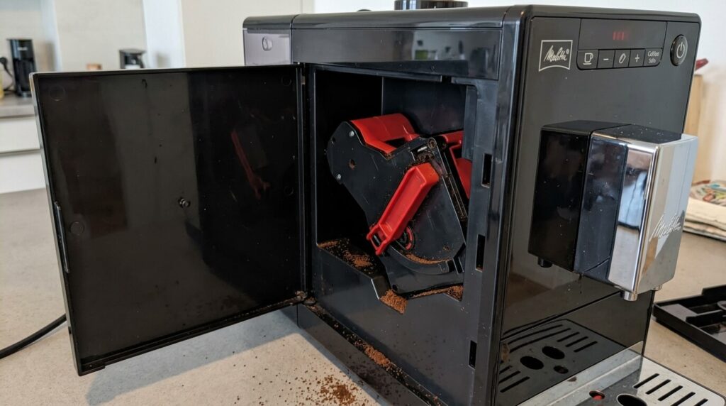Chambre d'extraction Melitta bloquée : comment la débloquer soi-même ? 2 L'ouverture latérale d'une cafetière Melitta montrant le groupe d'infusion rouge et noir coincé dans son logement.