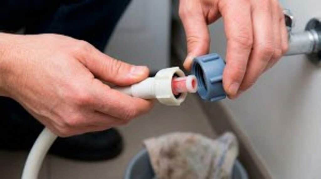 Voyant robinet qui clignote sur un lave-vaisselle Viva : causes et solutions 3 Une personne dévissant le tuyau d'alimentation en eau pour vérifier le petit filtre en plastique.