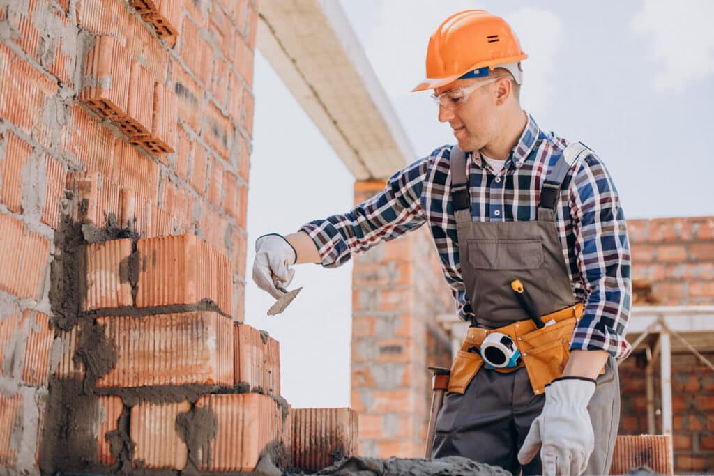 Propriétaire posant des briques sur le chantier de sa maison en auto-construction.