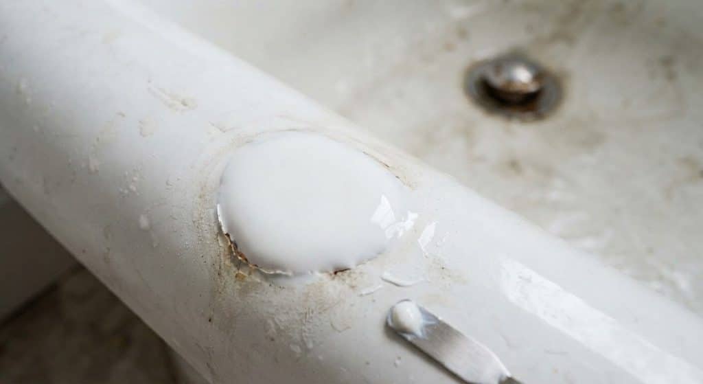 Rouille dans la baignoire : est-ce dangereux ? 3 Application d'une résine époxy blanche sur un point de corrosion pour restaurer l'étanchéité de la baignoire.