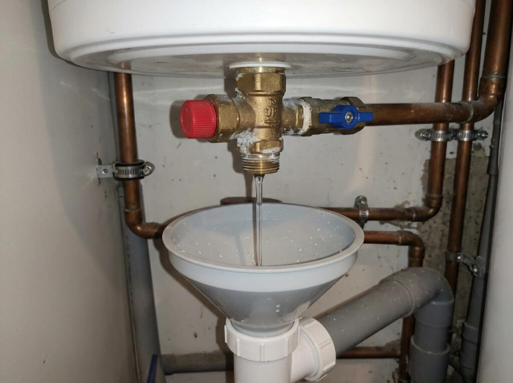 Filet d'eau continu s'écoulant par l'entonnoir du siphon sous un groupe de sécurité de chauffe-eau.
